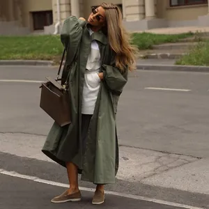 Oversized olive green long trench coat with lantern sleeves and side slits in street style