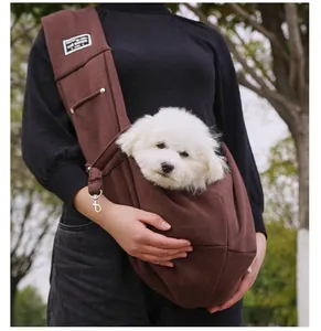 Close-up of a white puppy in a brown pet sling carrier worn by a person outdoors