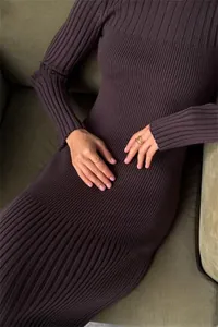 Close-up of dark brown ribbed knit dress on a model sitting on a sofa in detail