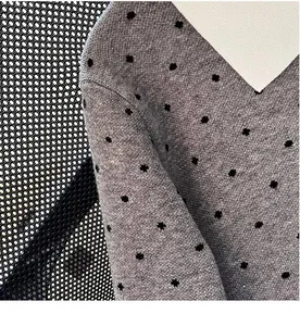 Close-up detail of grey knitted cardigan featuring black polka dot pattern and V-neckline.