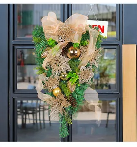 Elegant gold Christmas teardrop wreath with pine needles and festive ribbon on a glass door