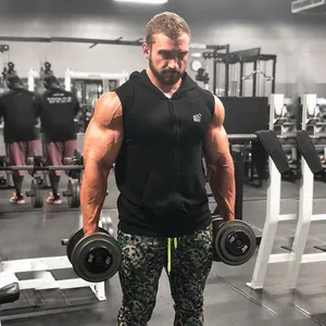 A muscular man showcasing a black sleeveless gym hoodie while training in the gym