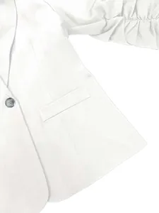 Détail d'un blazer blanc décontracté avec manches trois-quarts et bouton apparent.
