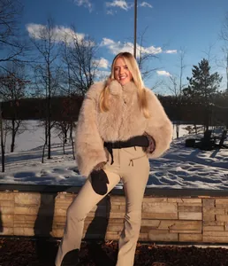 Woman in light khaki slim-fit ski suit and faux fur jacket posing in snowy landscape