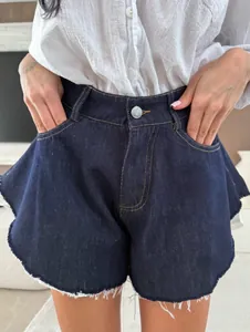 Dettaglio di pantaloncini di jeans blu scuro a vita alta con orlo a volant grezzo.