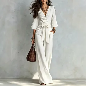 Lifestyle shot of white puff sleeve jumpsuit with waist bow belt and brown woven bag