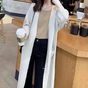 Detailed view of women's long thick knit cardigan sweater worn in a cozy cafe setting