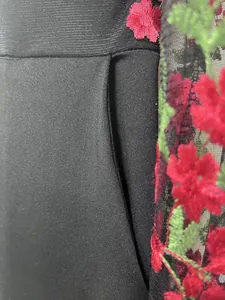 Primer plano detallado que muestra el bolsillo y el bordado floral rojo en malla negra