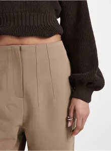 Detail view of high-waisted khaki trousers with pleated front and tailored waist design