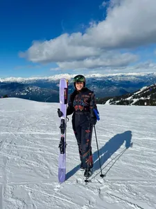 Woman wearing a floral embroidered ski jumpsuit standing on a sunny snow-covered mountain