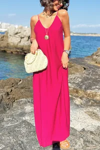 Model wearing a fuchsia spaghetti strap maxi dress standing against a rocky seaside backdrop