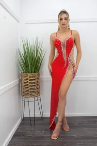 Full view of a red rhinestone sheer slip evening gown with a high slit on a model.