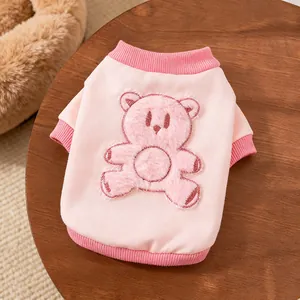 Nahaufnahme eines rosa Haustier-Sweatshirts mit flauschigem Bären-Patch auf Holz.