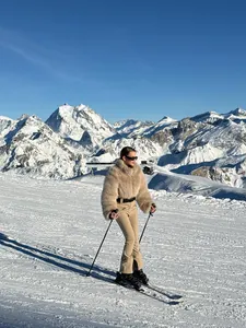 Woman wearing a khaki slim-fit ski suit with a faux fur jacket skiing on snowy mountains.