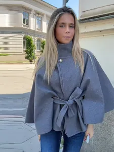 Primer plano de una chaqueta poncho gris con cinturón de talle y botón metálico.