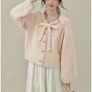 Primo piano di un cardigan rosa in maglia con un grande fiocco decorativo e bottoni floreali.