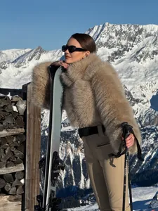 Woman in a luxury khaki ski suit and faux fur coat posing in snowy mountains