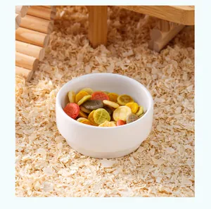 Bol en céramique blanc pour hamsters rempli de friandises sur des copeaux de bois.