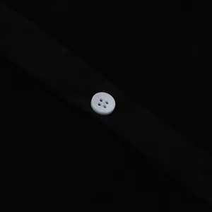 Close-up detail of a classic white four-hole button on black textured fabric garment