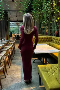 Back view of elegant burgundy ribbed knit bodycon maxi dress in restaurant setting