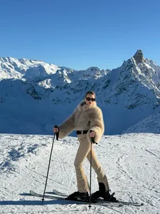Detailed view of women's beige faux fur jacket and flared ski pants in snowy mountains