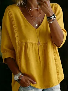 Detailaufnahme einer gelben V-Ausschnitt-Bluse mit Spitze und Dreiviertelärmeln.