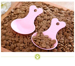 High-quality pink bone-shaped pet food scoop resting on small brown kibble pellets
