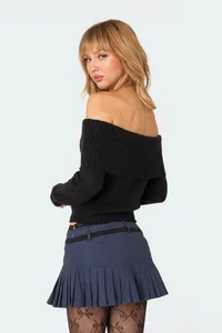 Back view of a black off-the-shoulder knitted sweater paired with a pleated mini skirt