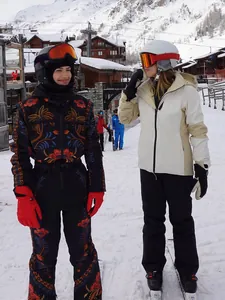 Two models posing in professional ski gear on a snow-covered mountain resort background