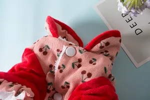 Detailopname van corduroy huisdierkleding met kersenprint, rode pluche bies en drukknoop.