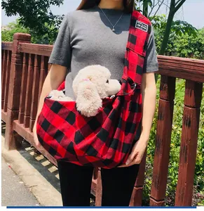 Detail view of red and black plaid pet sling carrier bag with adjustable strap worn outdoors