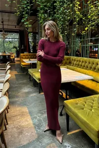 Model wearing a burgundy ribbed knit maxi dress while standing in a stylish cafe interior.
