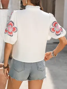 Detailed back view of white top with floral embroidered puff sleeves and ruffle neck.