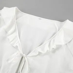 Macro view of a white cotton linen V-neck blouse featuring elegant ruffle details and a tie-front.