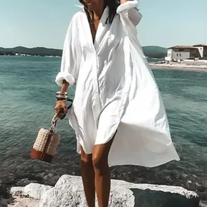 Elegante Frau in einem langen weißen Oversize-Baumwollhemdkleid am Strandufer.