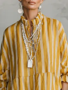 Primer plano de camisa suelta de rayas amarillas y blancas con collares en capas de moda