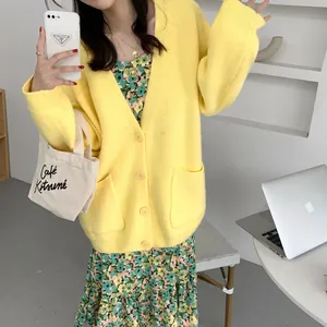 Close-up of a loose yellow knit cardigan worn over a floral dress in a casual setting