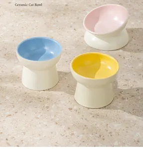Lot de trois bols surélevés en céramique pour chats avec intérieur coloré sur terrazzo.
