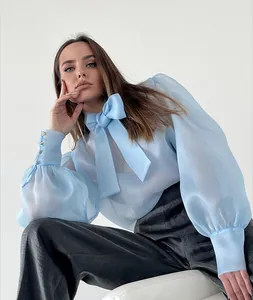 Elegante blusa de malla transparente azul claro con mangas abullonadas y gran lazo al cuello.