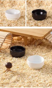 Bols en céramique noirs et blancs pour hamster dans une cage en bois avec copeaux.