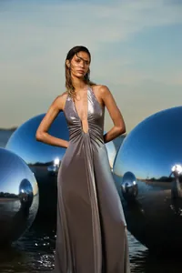 Model wearing a metallic silver halter dress standing among large reflective spheres