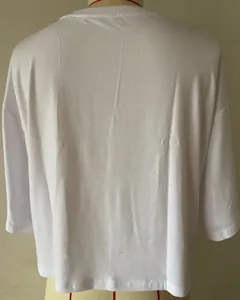 Λεπτομερής πίσω όψη λευκού κοντού T-shirt με διακριτικό ανάγλυφο σχέδιο CD στο πλάι