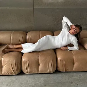 Detail of white long-sleeved ribbed knit dress worn by model on a modern tan leather sofa