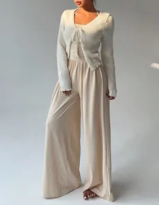 Detalle de un mono beige de pierna ancha con un cárdigan blanco de punto y cierre de lazo.