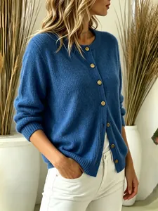 Close-up of blue knit cardigan with gold buttons worn by a model in a minimal setting.