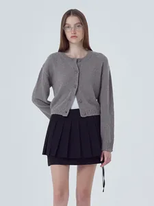 Full view of a woman wearing a grey knit cardigan and black pleated skirt outfit.
