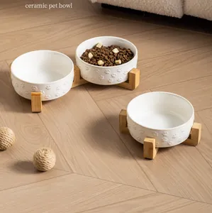Detail of white ceramic pet bowls with paw patterns on minimalist bamboo stands.