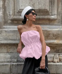 Elegant pink strapless peplum top with gathered waist, styled with a white hat and stone wall
