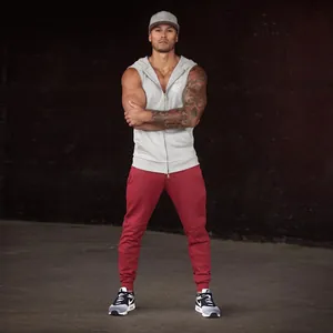 Full body view of a muscular man wearing a grey sleeveless gym hoodie and red joggers