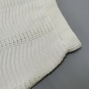 Detailed close-up of white knitted fabric featuring hollow wave patterns and ribbed edge